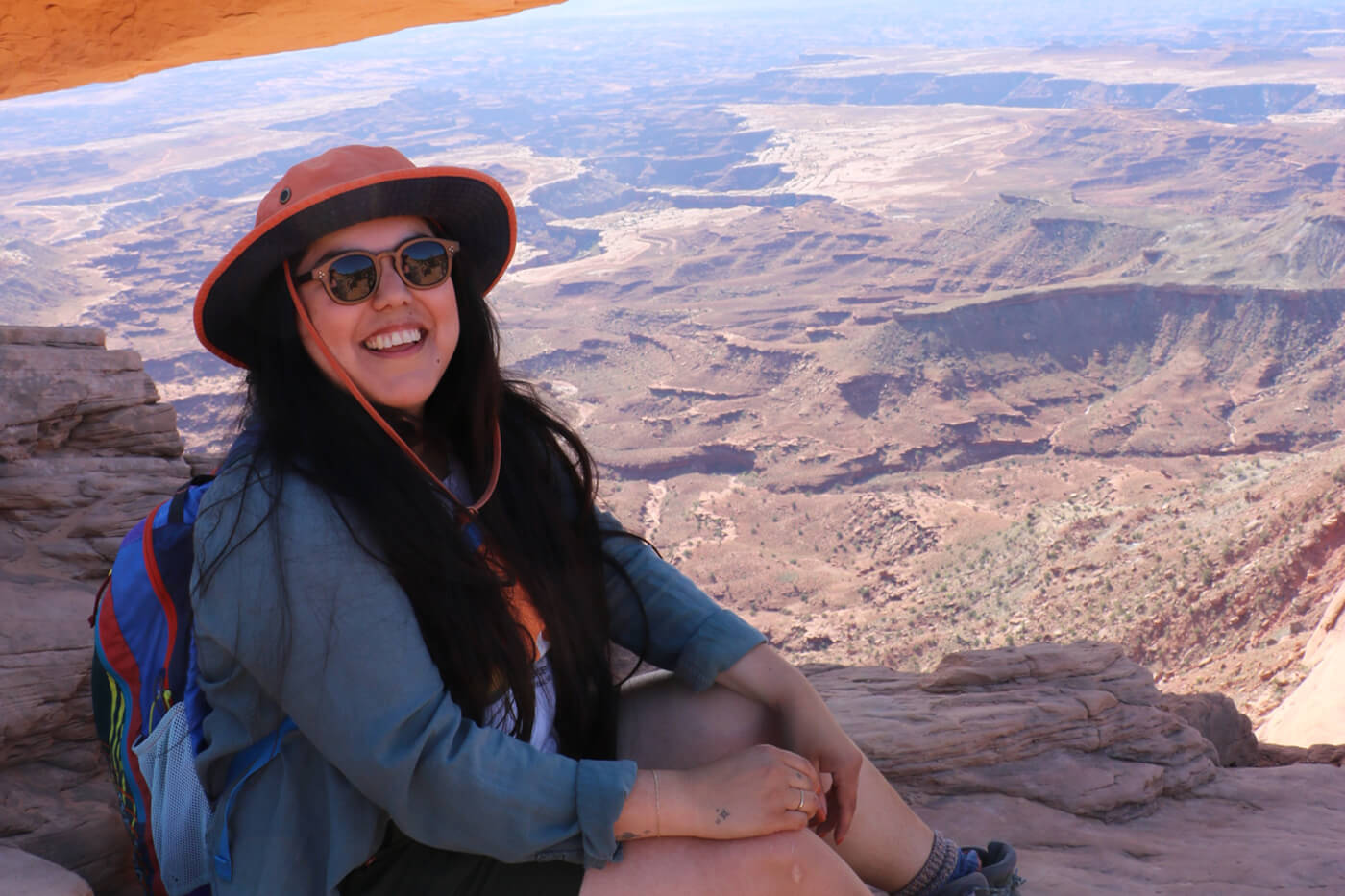 Cindy poses for a picture while sitting in front of a canyon of red rocks. 