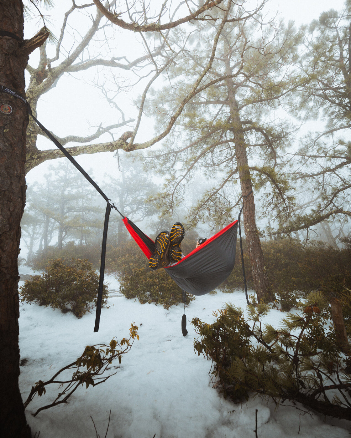 A man lays in an ENO hammock surrounded by fog and winter weather in the woods. 