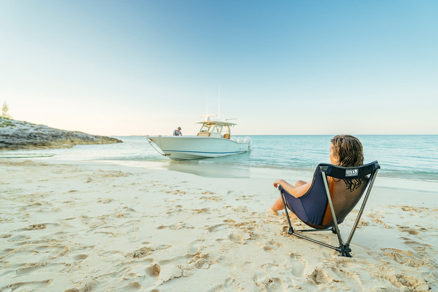 A woman sits in an ENO Lounger SL chair on the beach looking out on a boat. 