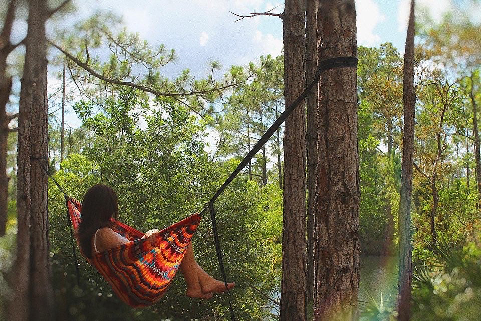 A woman sits in an ENO Hammock Print in a lush green forest. 