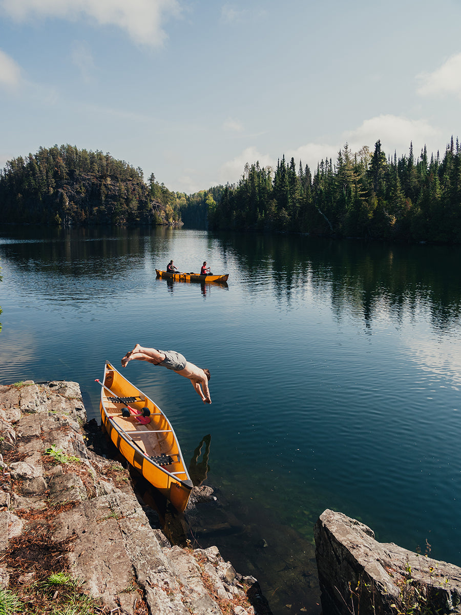 A man jumps into the lake with a canoe in the background while in the Boundary Waters Canoe Area Wilderness