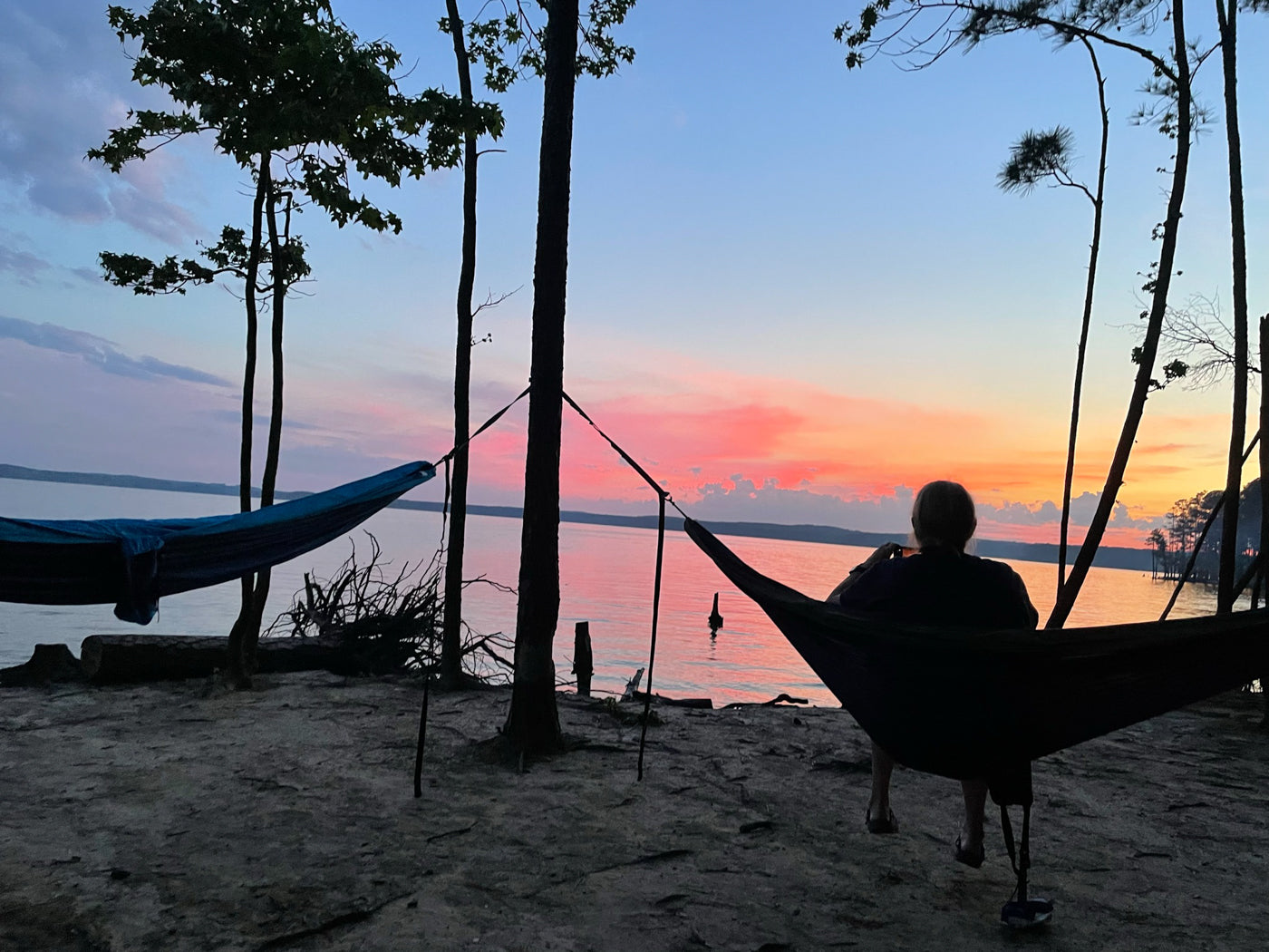 A person sits in an ENO hammock in front of a lake watching the sunset. 