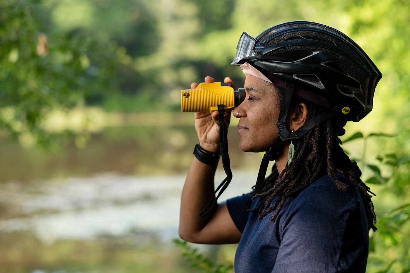 A woman wearing a bike helmet looks through binoculars while birding on a bike ride.