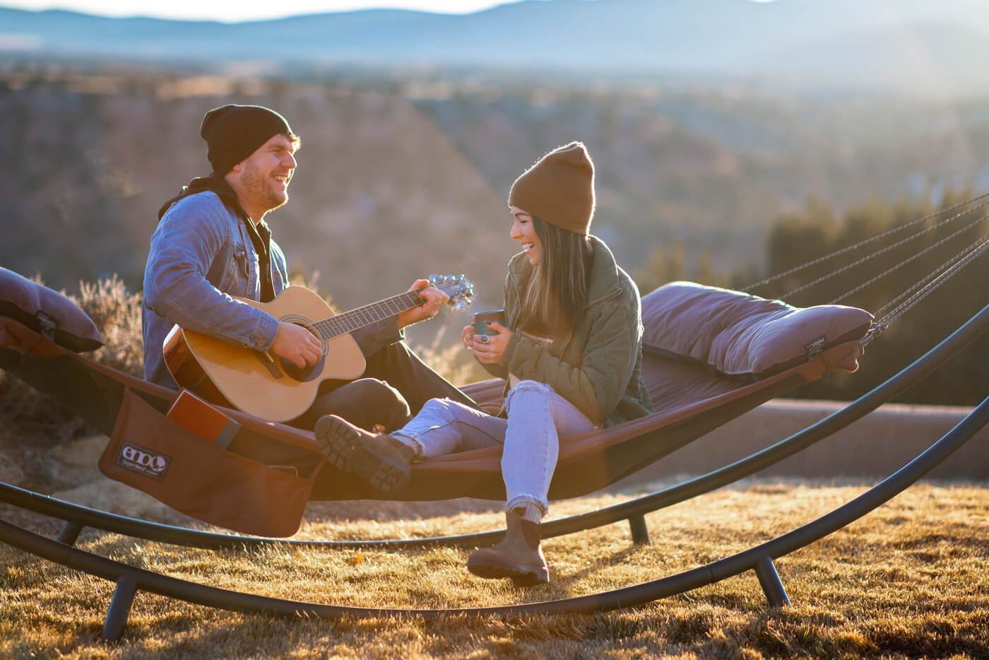 A couple sits in an ENO SuperNest Hammock with coffee and a guitar.