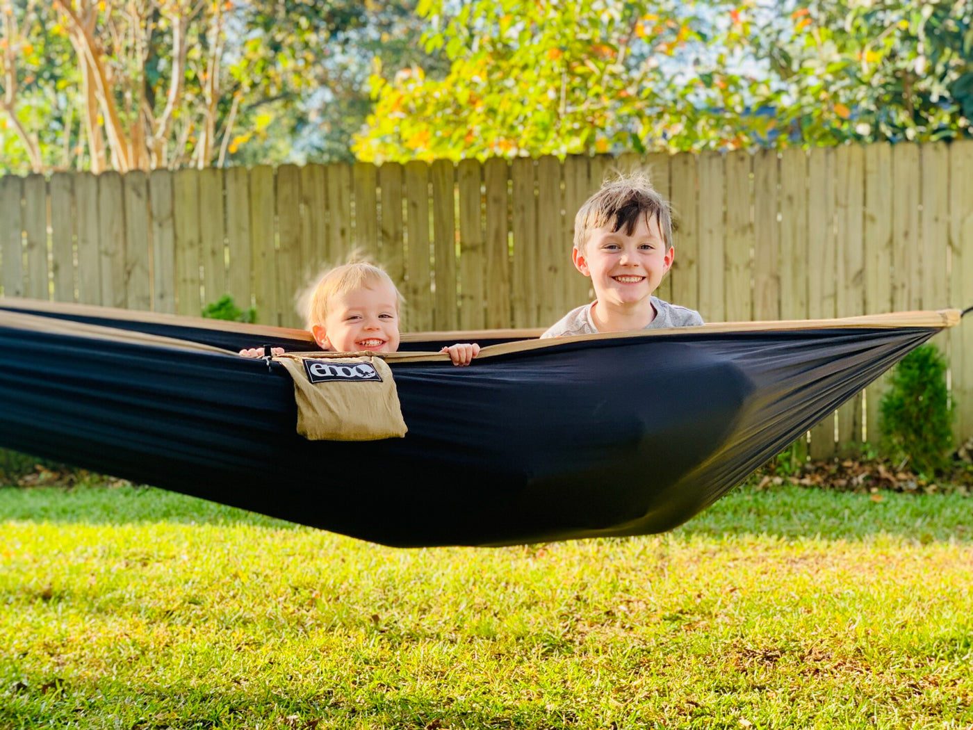 Two boys sit in an ENO hammock together in the backyard. 