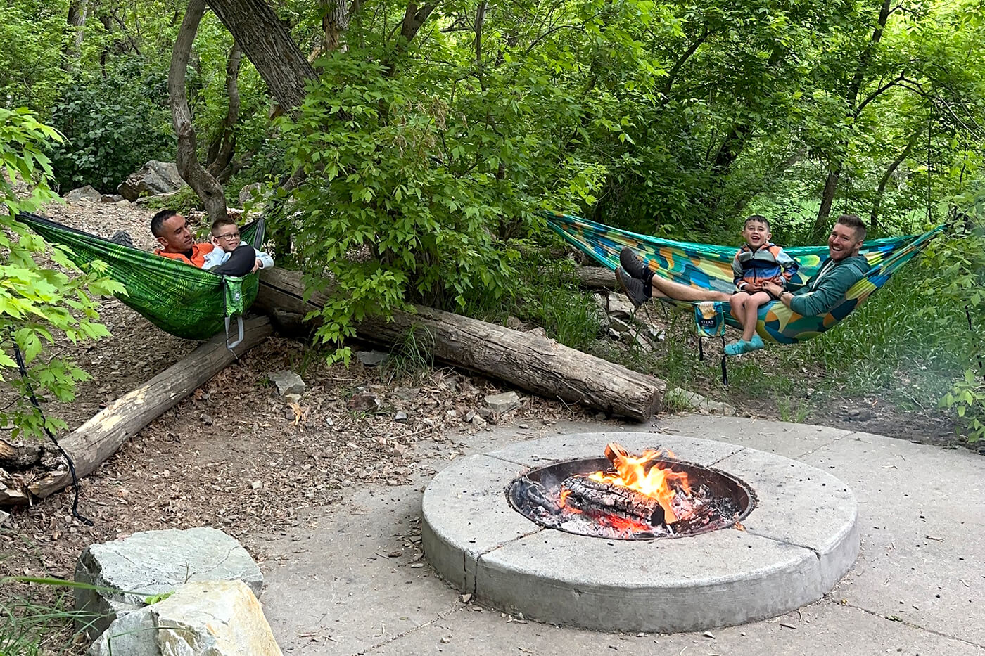 The Fontes family hammocks together around a fire pit in the woods.