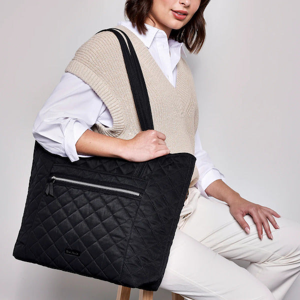 Model holding black quilted Vera Bradley tote bag