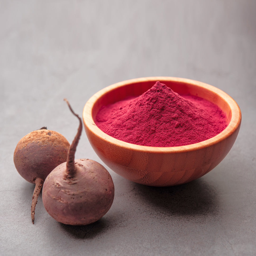 A powedered face mask is mixed into a bright pink paste in a small clear bowl with a small wood spoon.