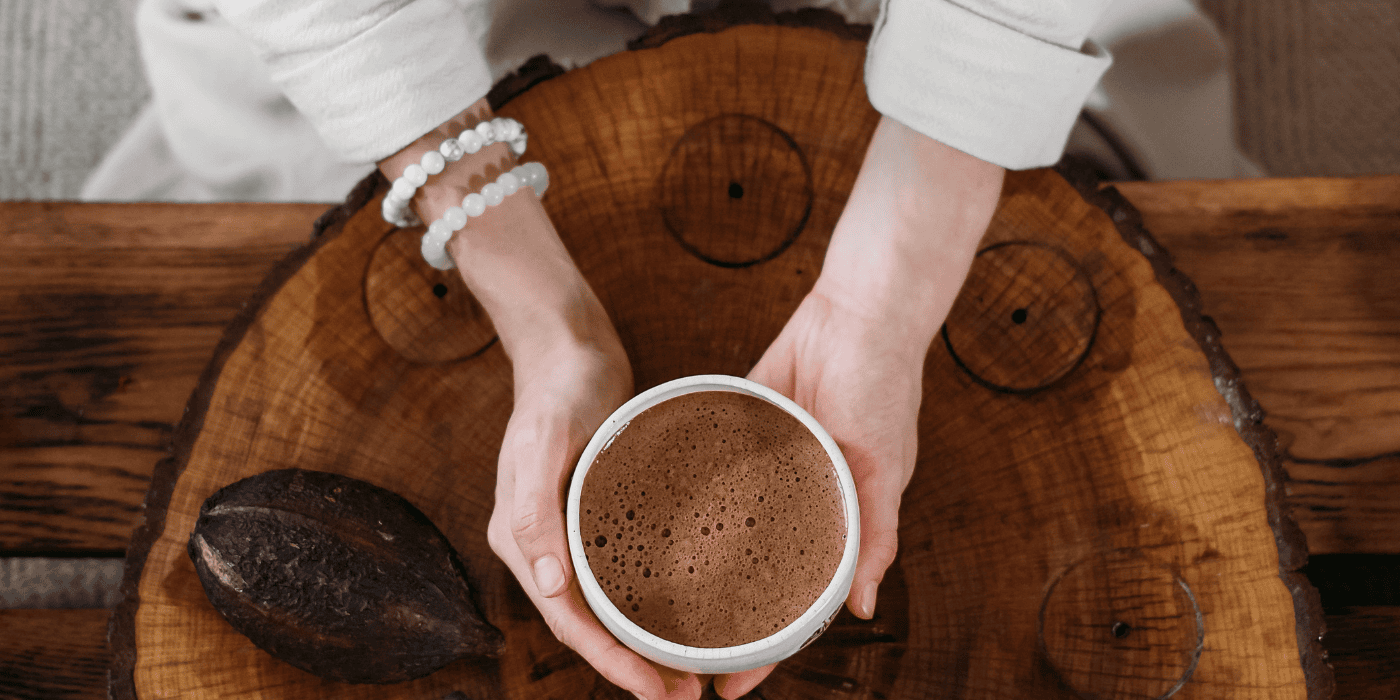 Von oben fotografiert, mit einer Tasse Kaffee in der Hand und neben der Hand eine Kakaobohne