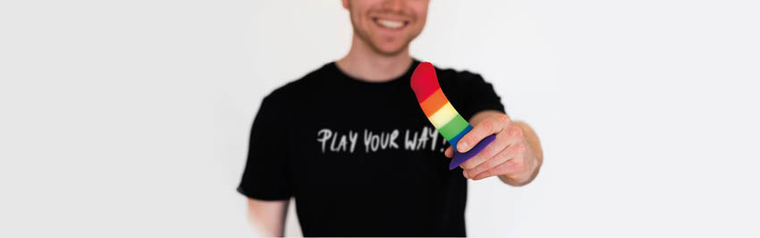 Glücklicher Mensch mit Dildo AMOR Rainbow in der Hand