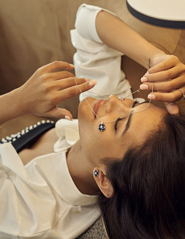 A model holding Pristi necklace and wearing Prtisti earrings with lab grown diamond and oval cut sapphire gem stones.