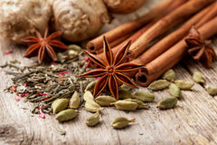 A collection of aromatic spices, including star anise, cinnamon sticks, cardamom pods, and ginger root, arranged decoratively on a light-colored wooden surface
