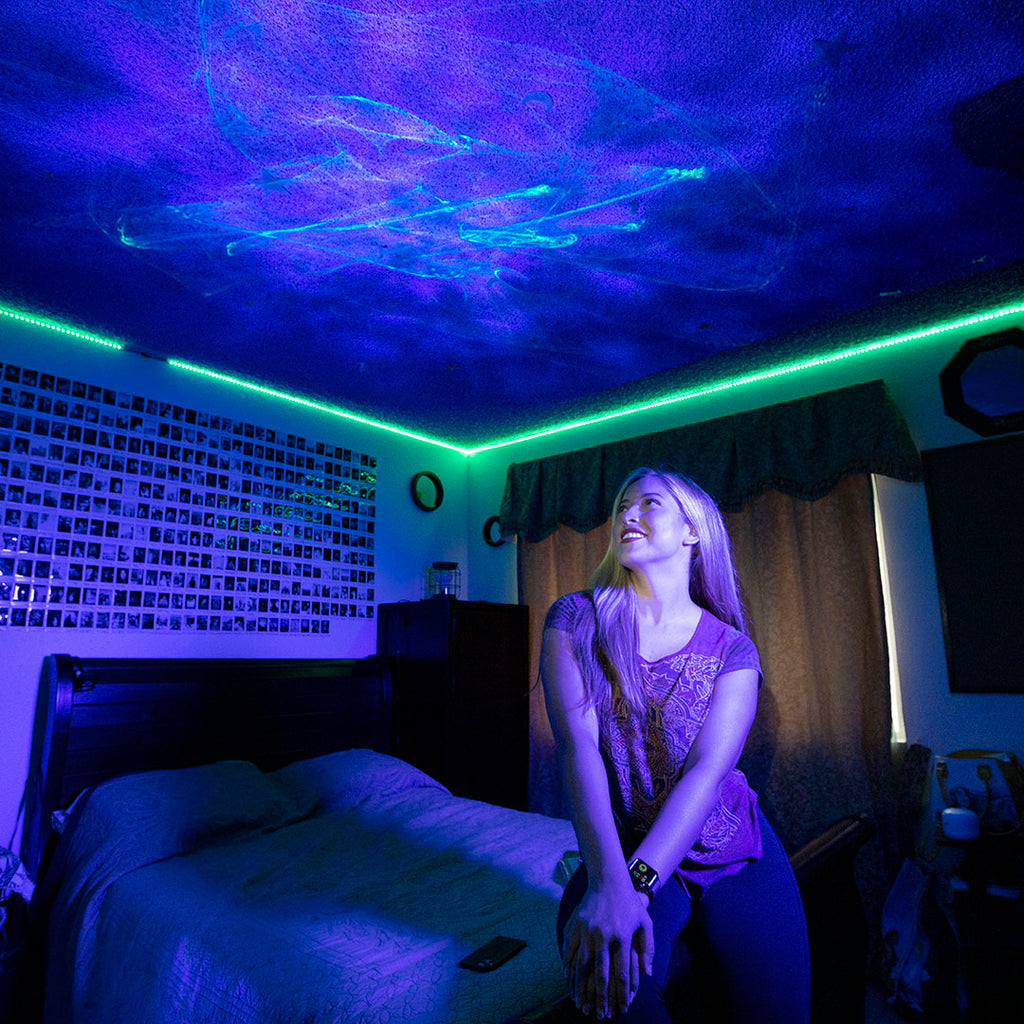 woman sitting on bed looking at ark aurora light on ceiling