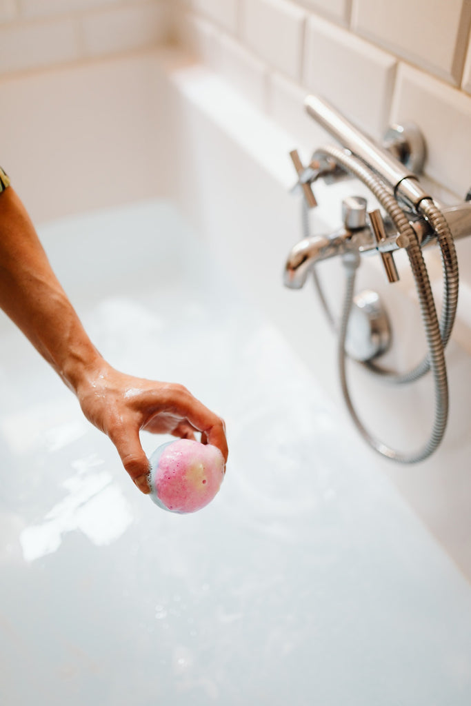 hand holding a pink bath bomb above tub