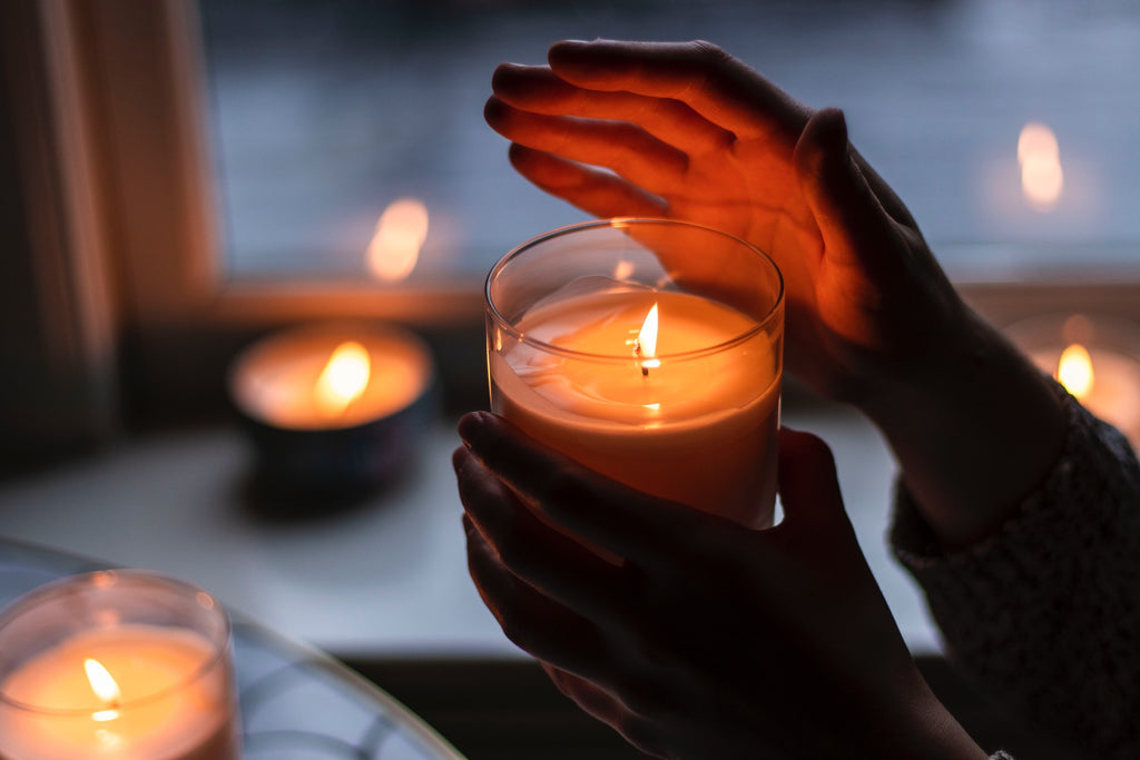 person holding a candle in a glass jar surrounded by more candles