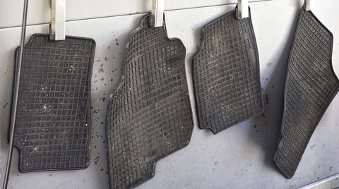 Four rubber car mats hang up on a line.