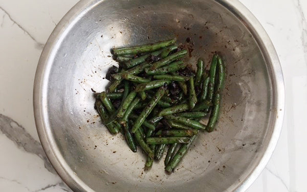 Squeeze 1½ heads of black garlic cloves from cut heads over green beans, then micro plane fresh garlic, sprinkle red pepper flakes and drizzle olive oil over veggies and gently toss to combine. 