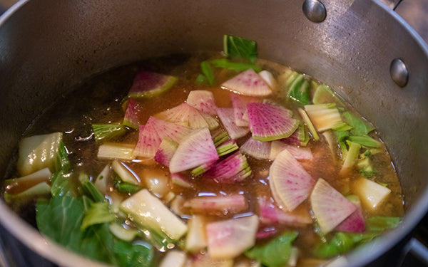 After the broth has simmered, add in the edamame, baby bok choy, and watermelon radishes and cook for 5 minutes or until the vegetables are tender. 