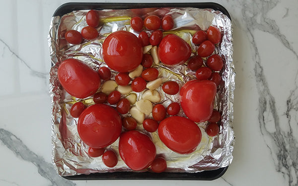 Line a baking sheet with foil and place tomatoes and garlic in pan, then sprinkle with salt and pepper. Place in oven and roast for 1 hour or until the tomatoes and garlic are soft and lightly browned.