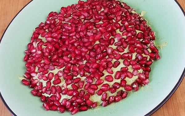 Center cheese mixture on a large serving plate and cover in pomegranate arils, line with whole grain crackers and serve.