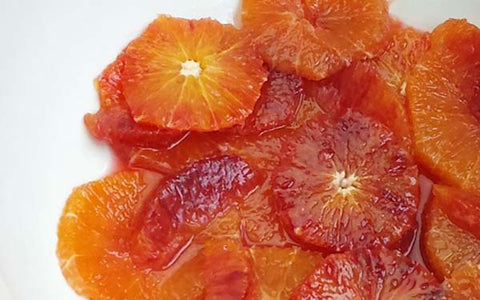 Image of Working over a medium bowl, cut between membranes of two of the blood oranges to release segments into bowl. Slice the remaining blood orange and Cara Cara crosswise into thin rounds. Place the sliced oranges into the bowl with the segments, add lemon and lime juice