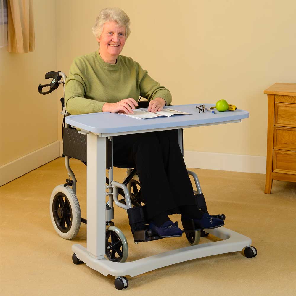 An individual in a wheelchair using a pale blue over-chair desk.