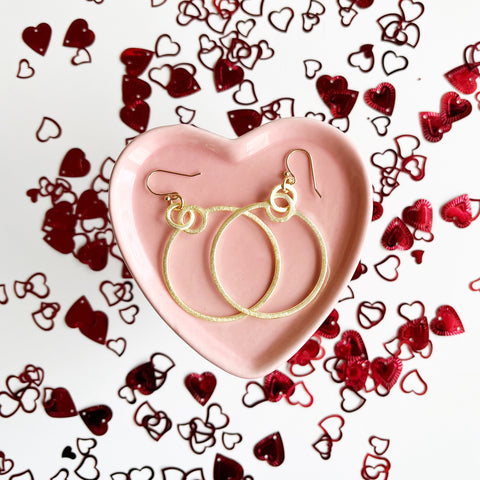 gold hoop earrings in pink heart dish surrounded by red heart confetti