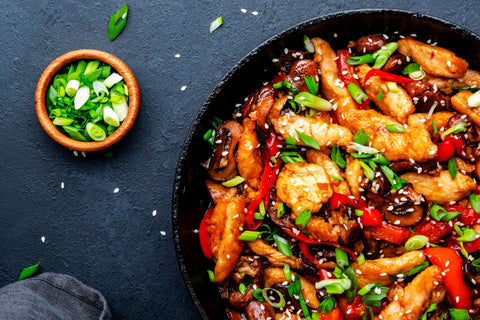 Asian cuisine stir fried chicken, paprika, mushrooms, chives with sesame seeds in frying pan