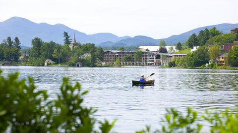 Photo of Person Kayaking in Lake with Buildings in Background 