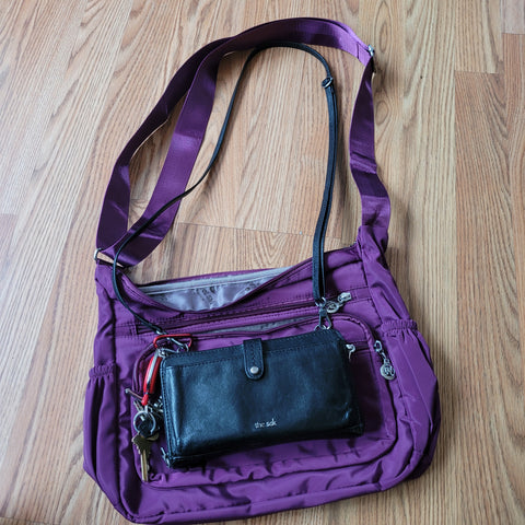 Image of Lisa's everyday black purse on top of the larger purple travel bag that she will use.