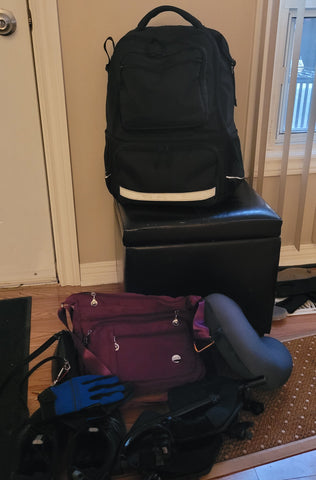All of Lisa's things ready to go by the door, including her black wheelchair backpack, purple crossbody bag, blue wheelchair gloves, wheelchair foot rests, and neck pillow.