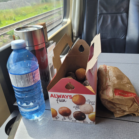Timbits (donut holes), a water bottle, a Contigo travel mug and a brown paper bag on a table.