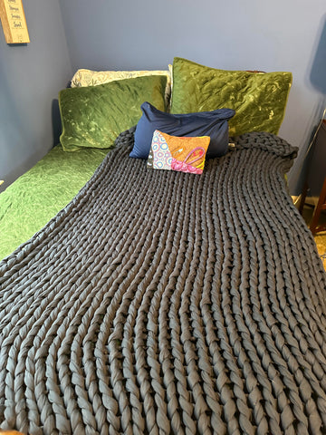 Gray Bearaby weighted blanket stretched out on a bed with a green comforter and pillows.