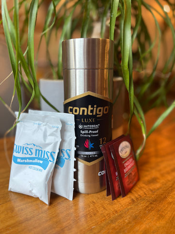 A silver Contigo Luxe Autseal travel mug on a table with hot chocolate packets and tea bags.