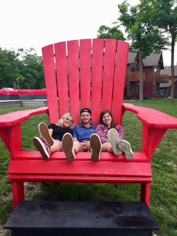 Ellie (right) sitting on a giant, oversized red launch chair with two friends. Their feet barely reach the edge of the seat.