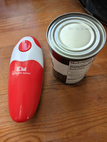 Red and white Kitchen Mama 2.0 Electric Can Opener, with one large red button toward the front of it and a small Kitchen Mama logo