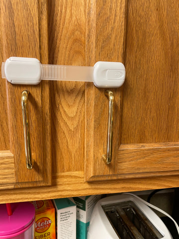 White Skyla Homes Baby Lock strap is stretched across two cabinet doors and secured on either side.