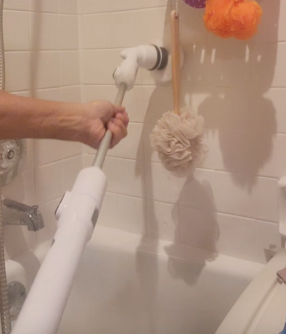 Extended power scrubber being held across a bathtub to scrub a shower wall.