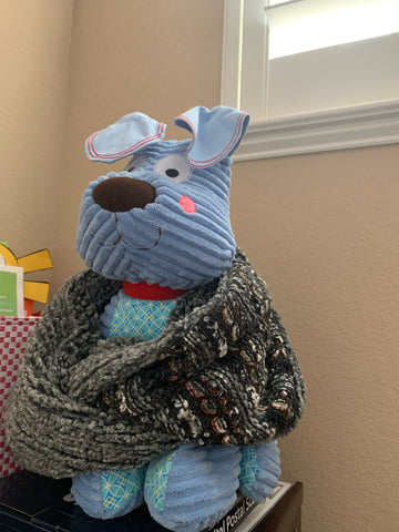 A blue stuffed animal dog is wearing a gray knit loop scarf.