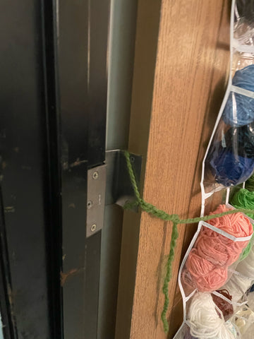 A close-up of green yarn wrapped around the door hinge.