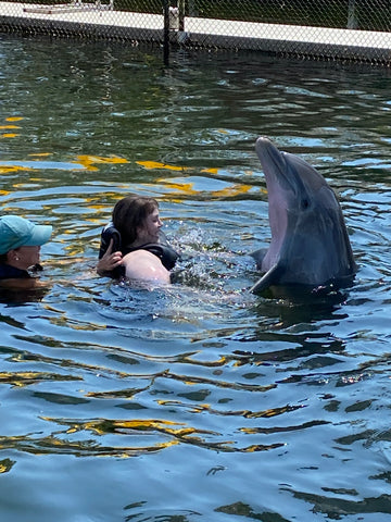 Jessica swimming with a dolphin that is popping up out of the water.