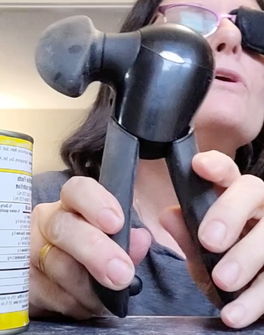 A woman is holding the two handles of a black OXO Good Grips Can Opener with a large black knob on the side.