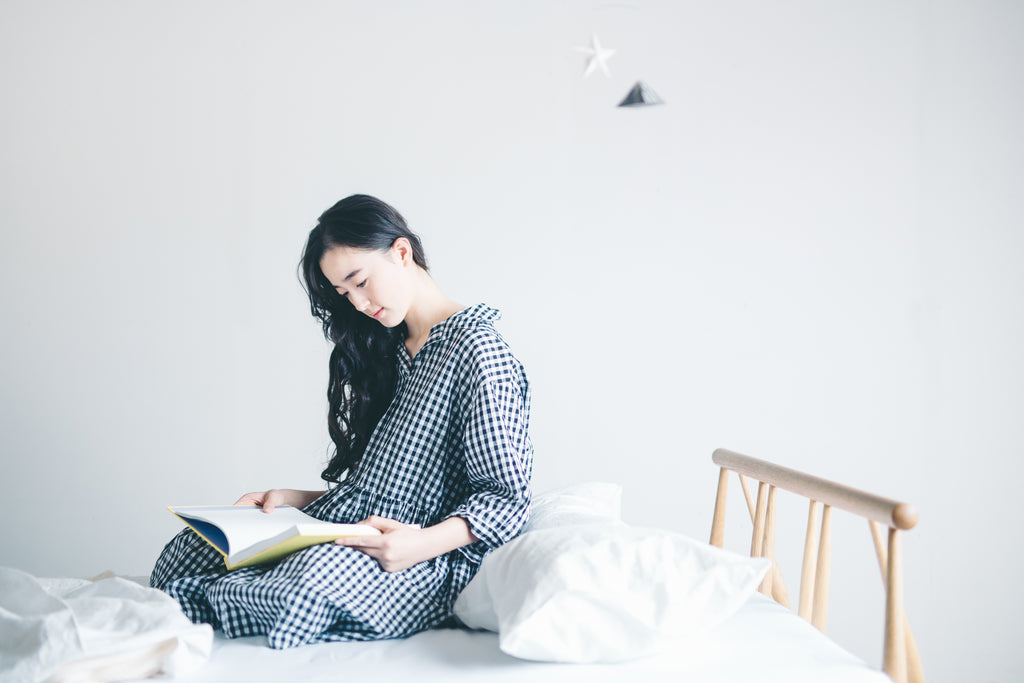 すっきりとしたヘッドのフラックスベッドの上で読書する女性