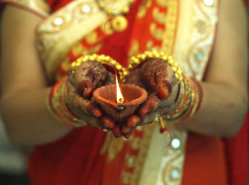 A woman holds a lit diya in her hands during Diwali