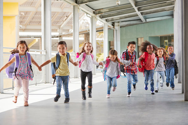 Happy children holding hands and running down a school corridor