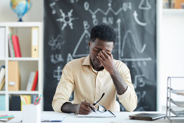 Young male teacher sat at desk looking tired