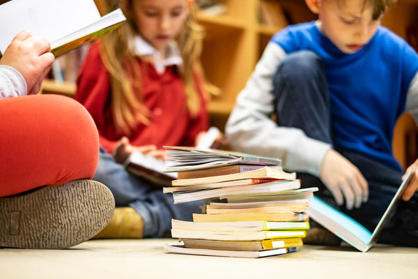 Pile of books with children reading in background