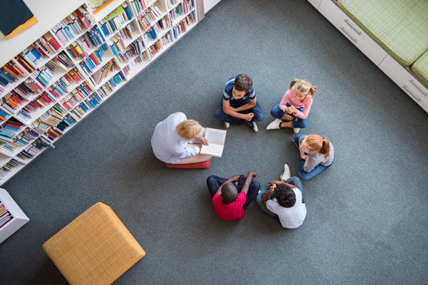 Children sitting in a circle being read a story by an adult.