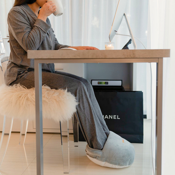 Woman using a foot warmer under desk while she is working and drinking coffee