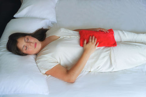 woman applying an electric hot water bottle on her belly to alleviate menstrual cramps